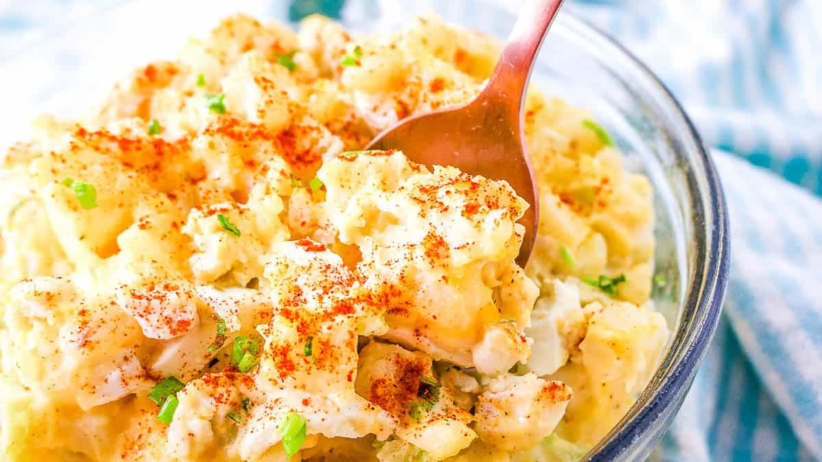 A bowl of creamy potato salad with egg garnished with paprika and chopped herbs.