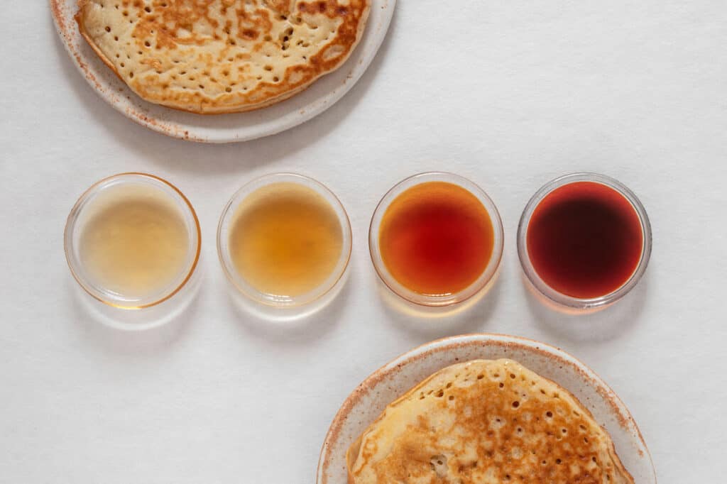 Pancakes with various liquids on a white surface, such as maple syrup.