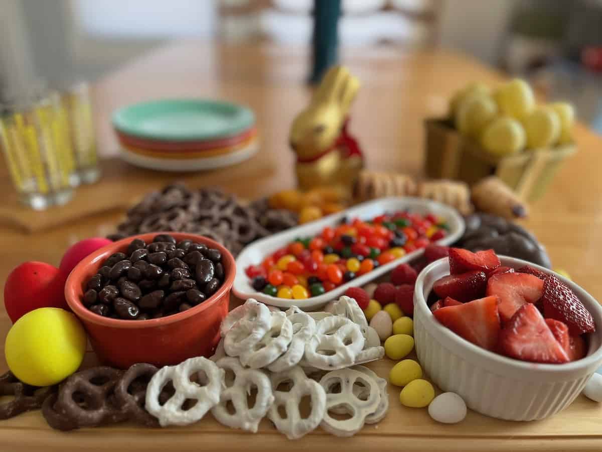 Easter candy charcuterie on a wooden board with plates and glasses in background.
