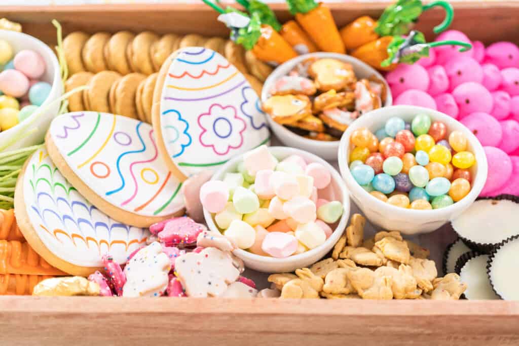 Assorted easter treats and colorful candies displayed in a wooden tray.