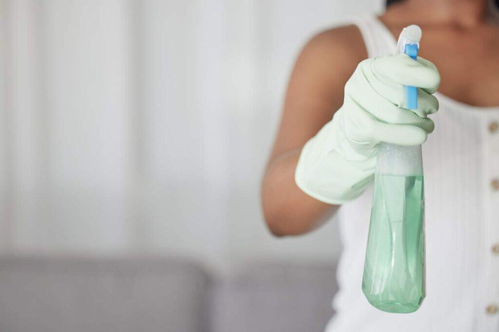 Person wearing gloves holding a spray bottle filled with eco-friendly cleaning products, ready for cleaning.