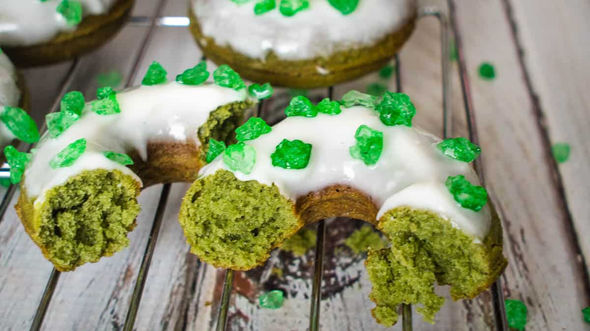 Green donuts with white glaze and green sprinkles on a wooden surface.