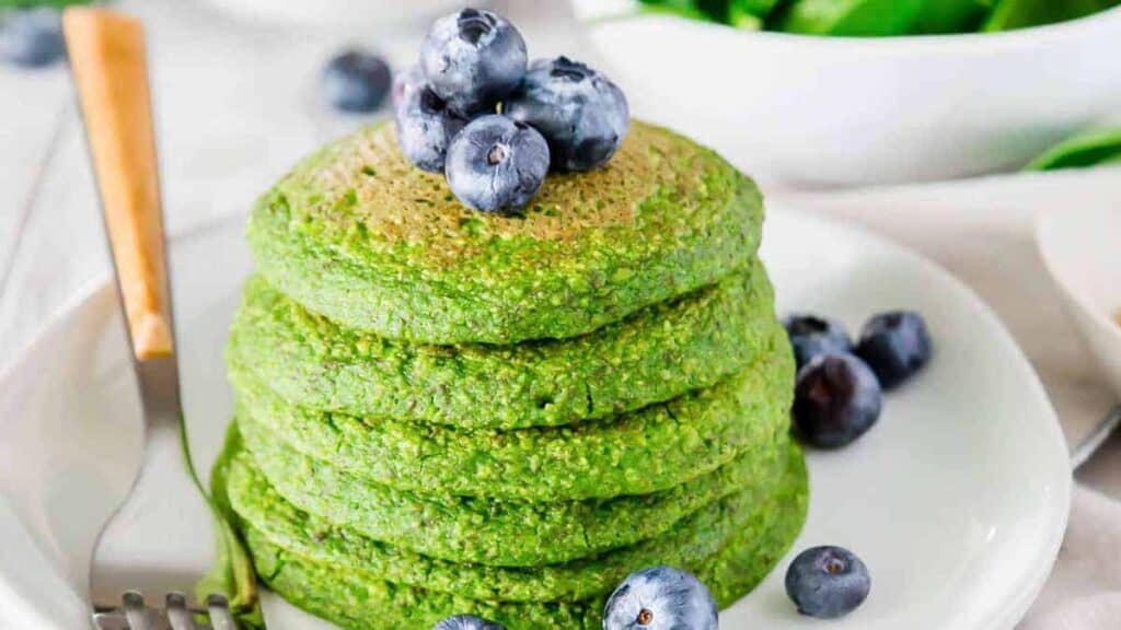 A stack of green spinach pancakes topped with fresh blueberries.