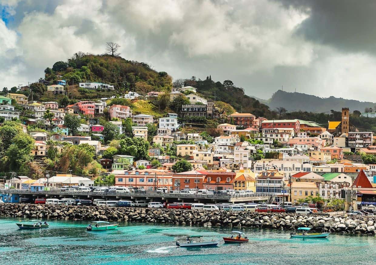 Colorful buildings on a hillside by the sea with boats in the foreground and a cloudy sky above.