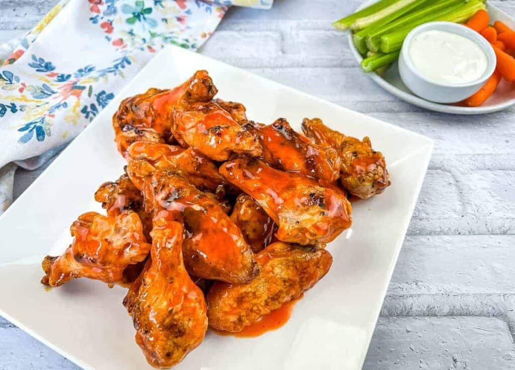 A plate of grilled wings with buffalo sauce served with celery sticks and ranch dressing.