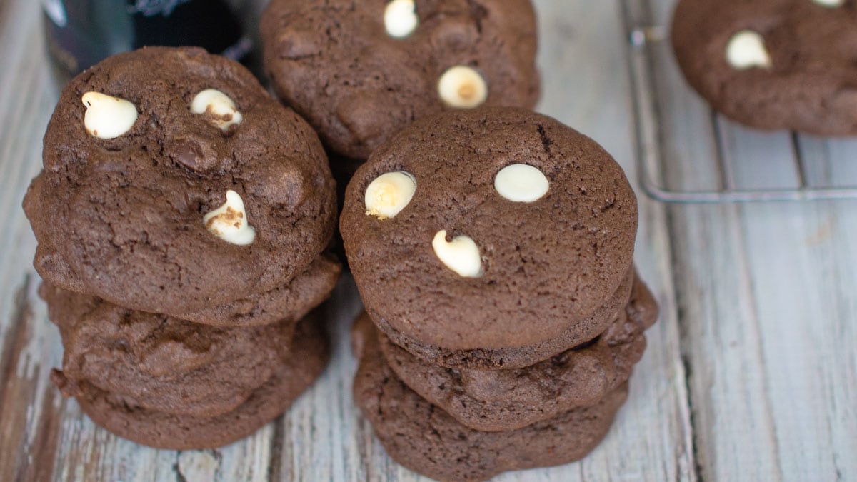 Stack of chocolate cookies with white chocolate chips on a wooden surface.