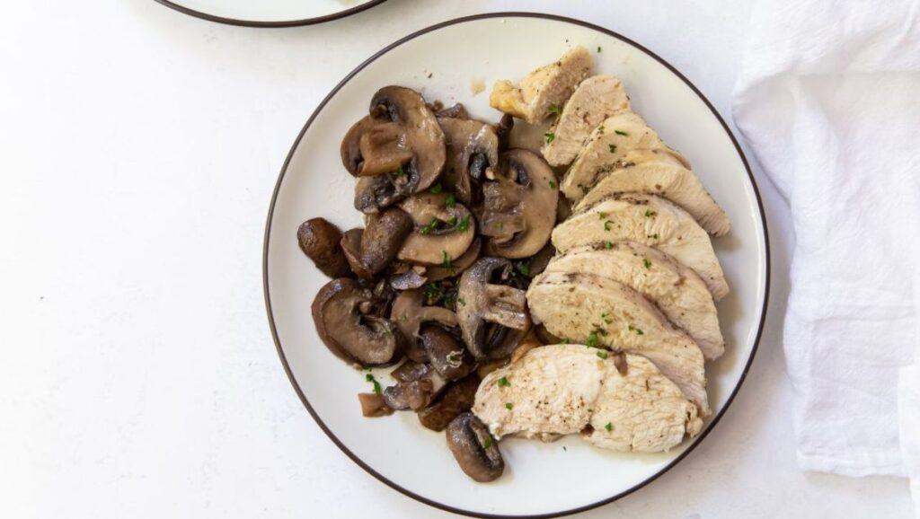 Sliced chicken breast and sautéed mushrooms on a plate.