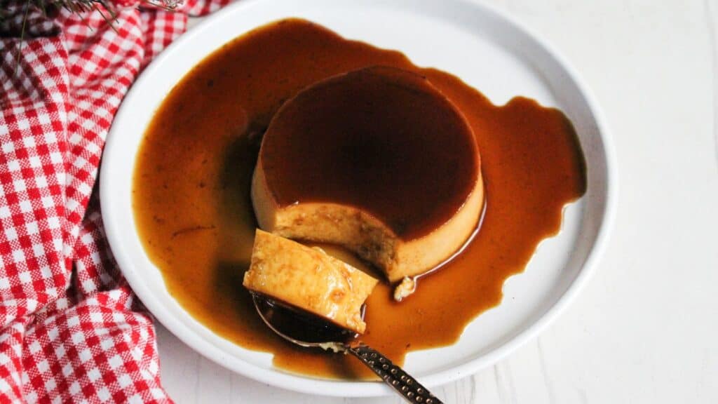 Caramel pudding served on a white plate with caramel sauce drizzled over it.