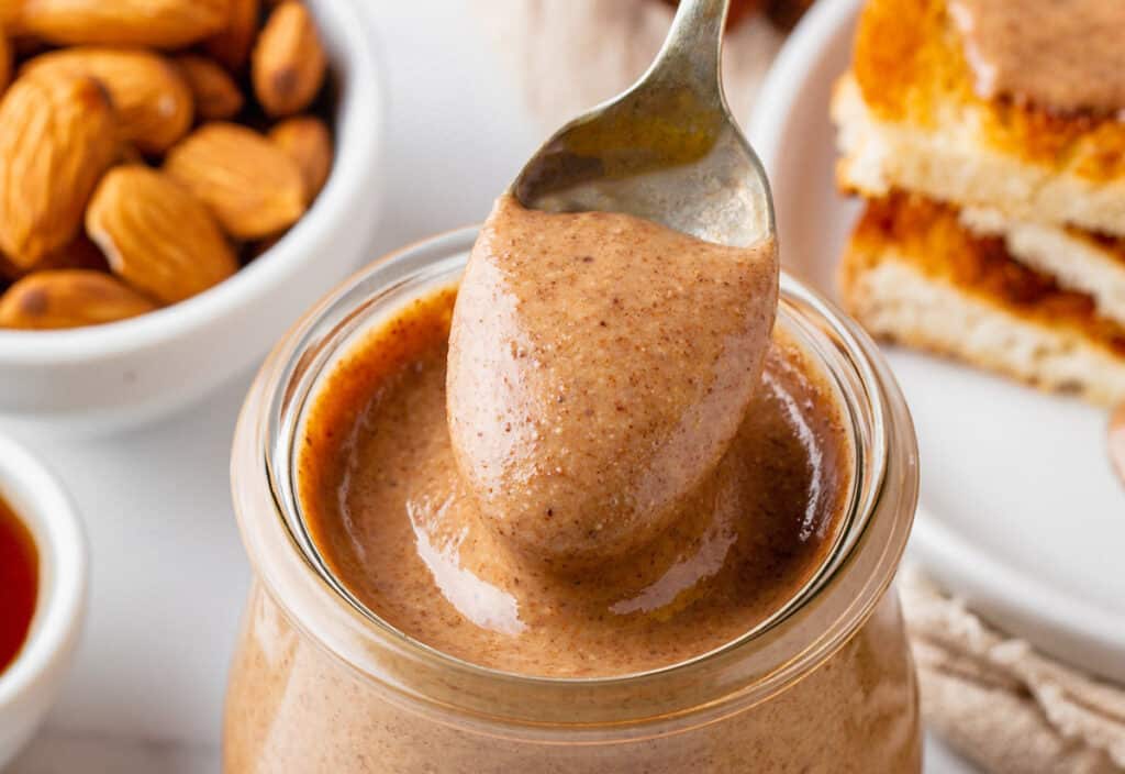 A jar of almond butter with a spoon and a slice of bread.
