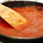 A pan of marinara sauce with a wooden spatula.
