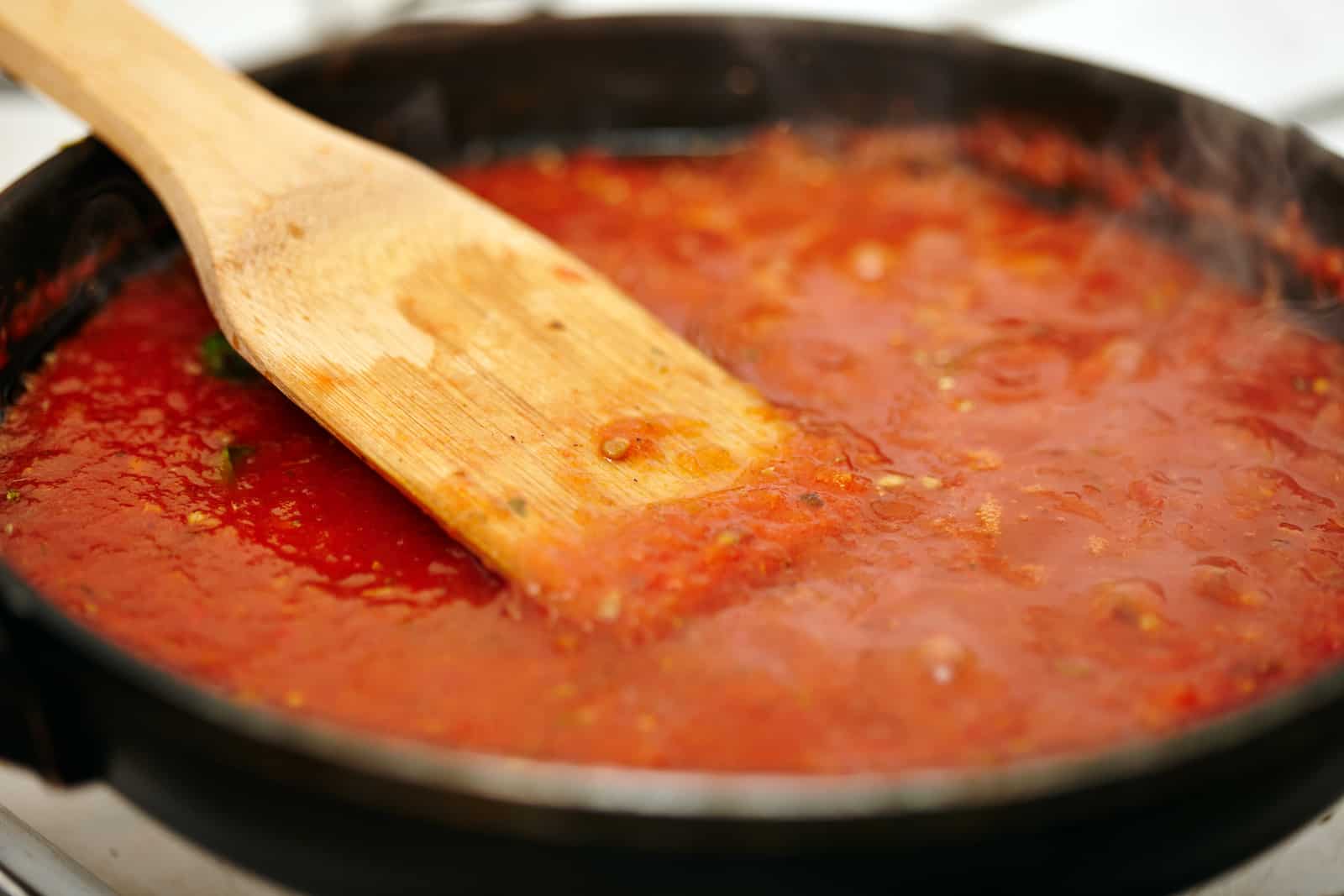 A pan of marinara sauce with a wooden spatula.