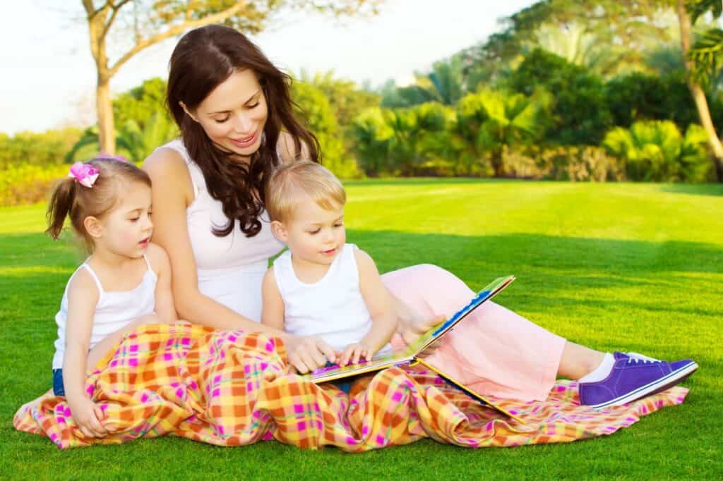 A woman is reading a book to her children in a park.