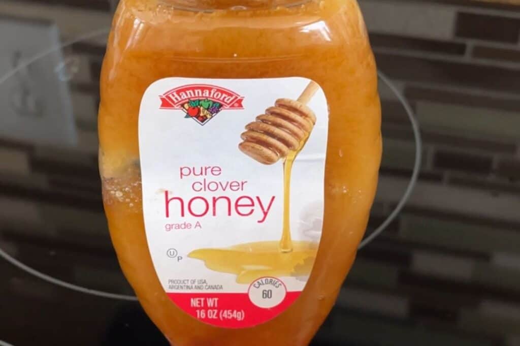 A jar of Hannaford brand grade A pure clover honey, decrystallized, on a countertop.
