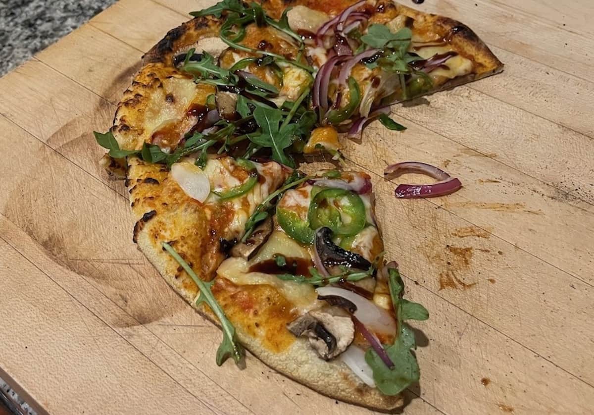 Sliced gourmet pizza with arugula and balsamic glaze on a wooden board.