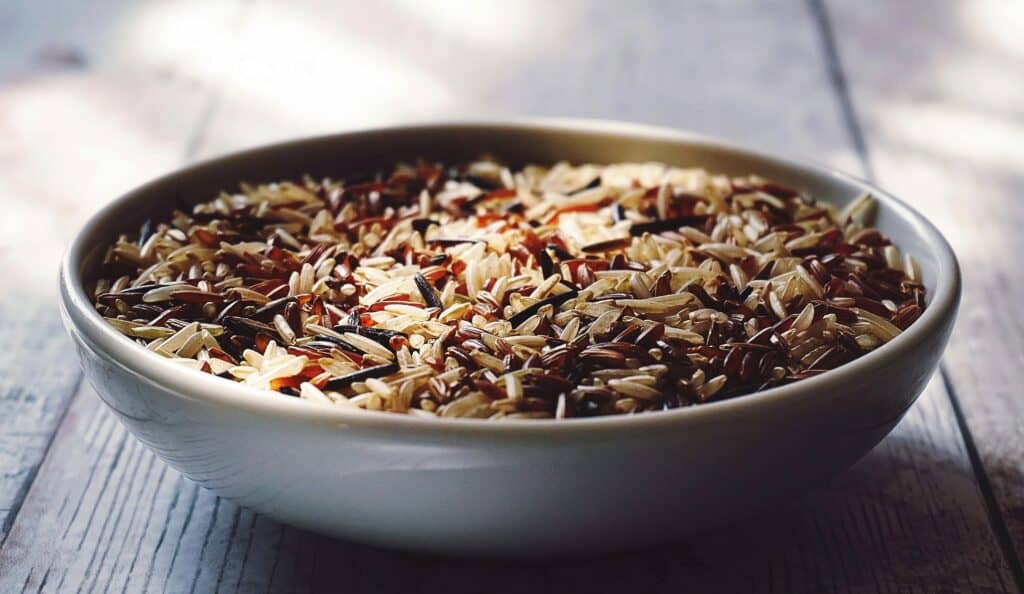 A bowl of mixed wild rice on a wooden surface.