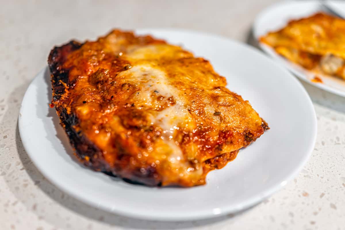 A slice of freshly baked lasagna with melted cheese on a white plate.