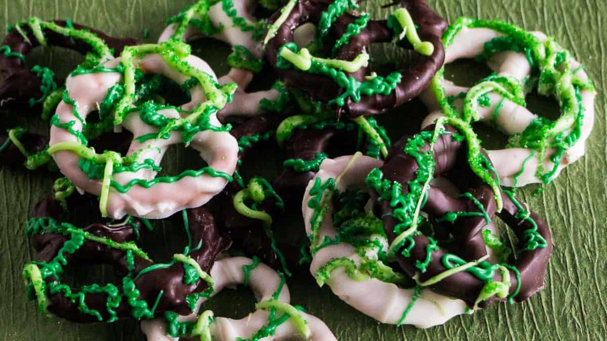 Chocolate-dipped pretzels with green sprinkles on a green surface.