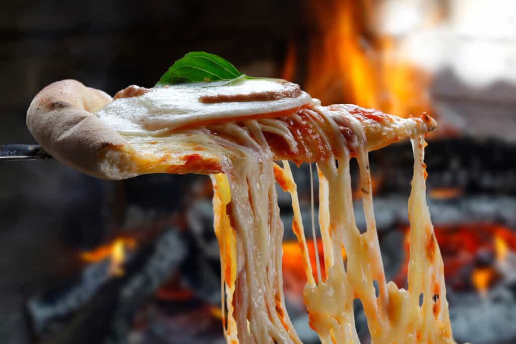 A slice of pizza is being held up by a fork in front of a fireplace.
