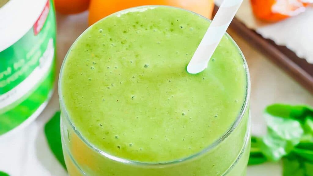 A green smoothie with a straw and oranges.
