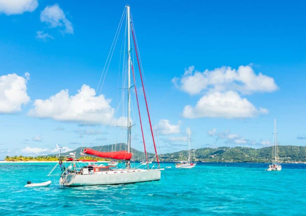 Sailboat anchored in clear turquoise waters with other boats in the distance under a bright blue sky.