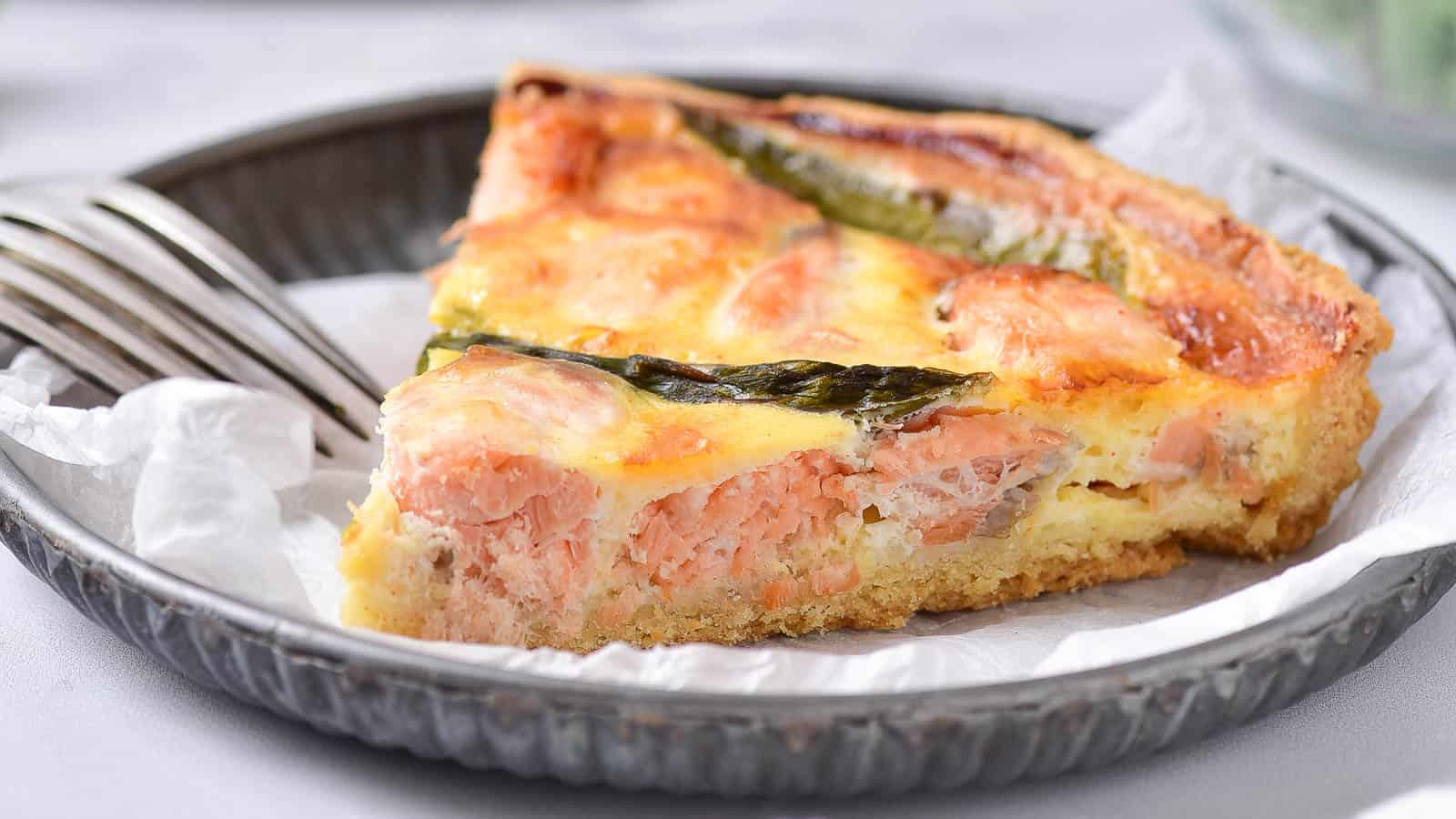 Salmon and asparagus quiche on a metal plate with parchment paper.