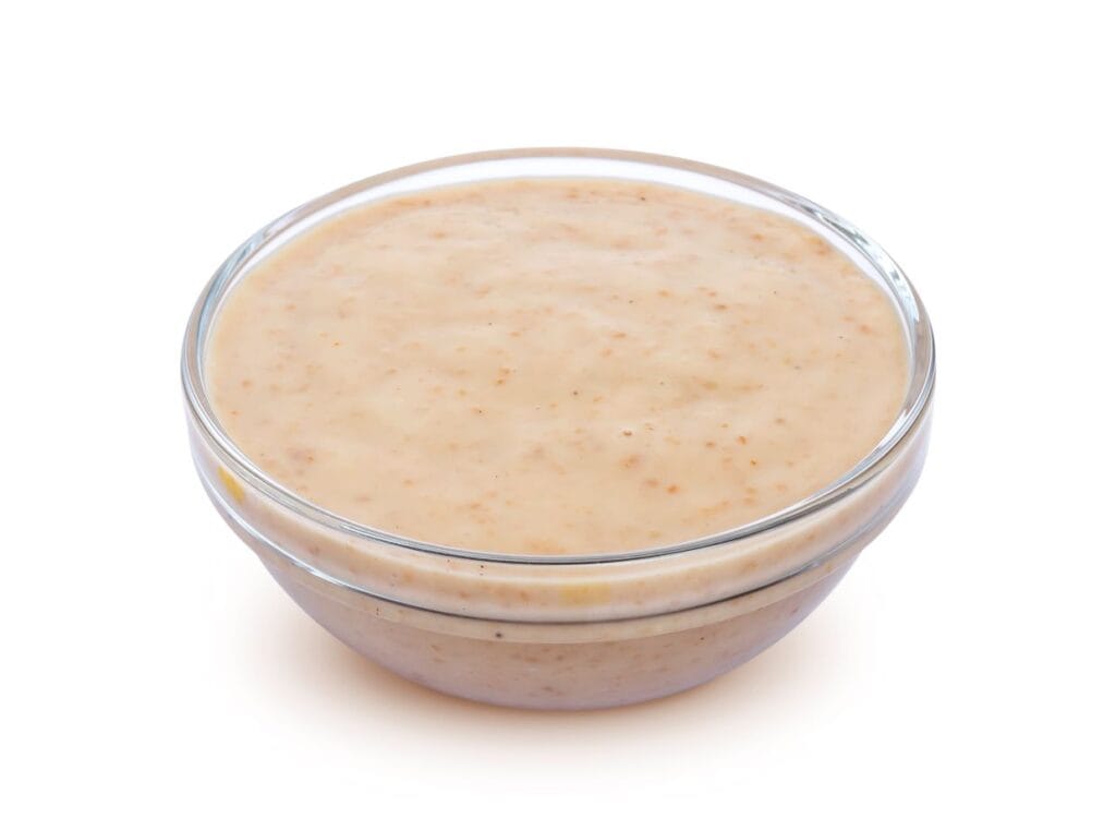 Bowl of creamy sauce with visible spices, isolated on a white background.