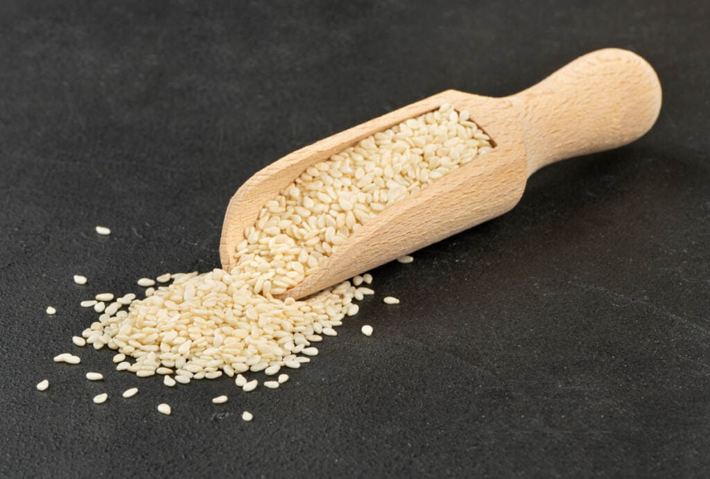 Sesame seeds in a wooden scoop on a black background.