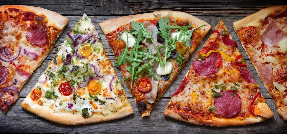 Five assorted pizza slices arranged side by side on a wooden surface.