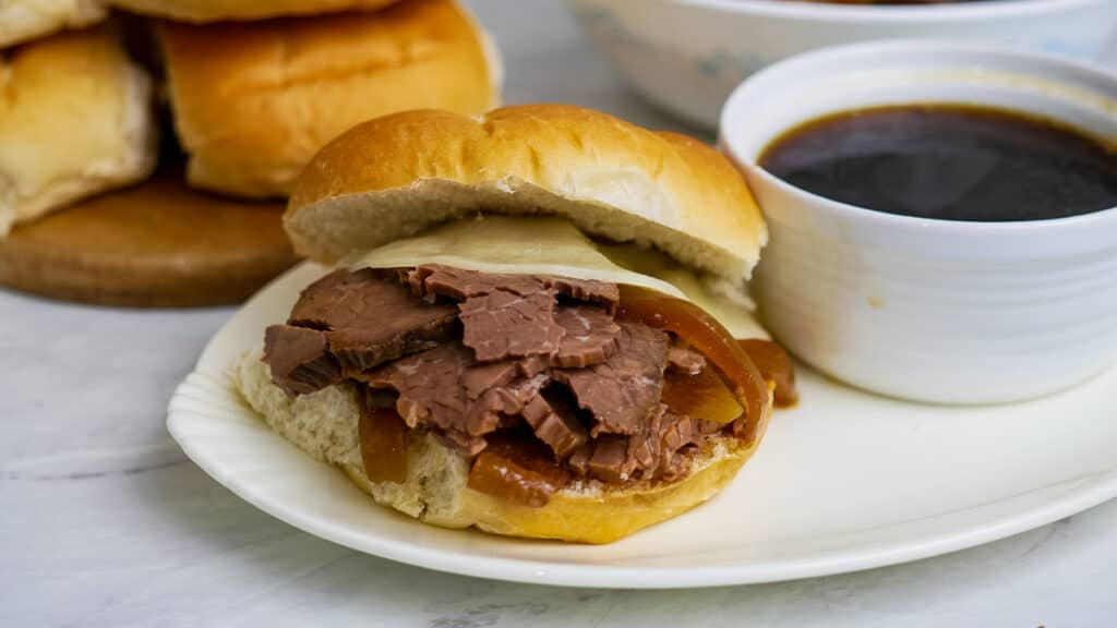 Roast beef sandwich with melted cheese and caramelized onions, served with a side of au jus sauce.