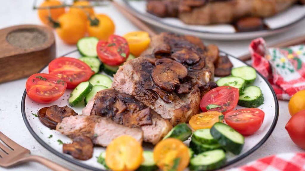 Grilled pork topped with mushrooms accompanied by a fresh salad of tomatoes and cucumbers.
