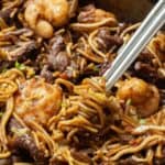 Stir-fried noodles with shrimp and beef in a pan with chopsticks.