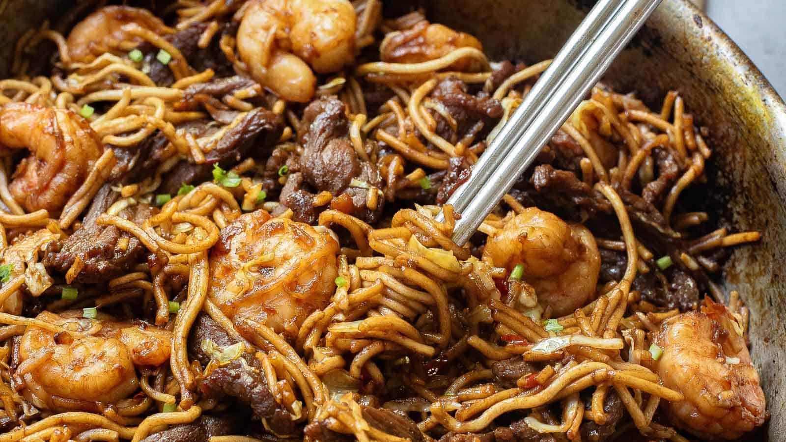 Stir-fried noodles with shrimp and beef in a pan with chopsticks.
