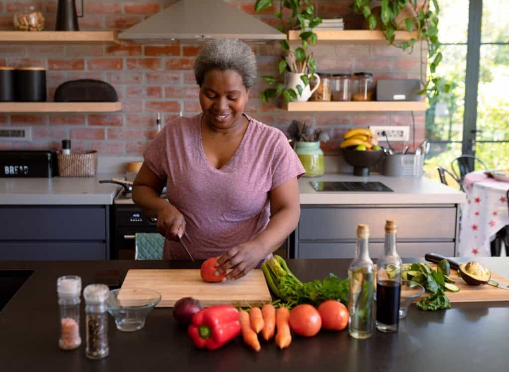 A woman slicing a tomato in a modern kitchen with vegetables on the countertop.