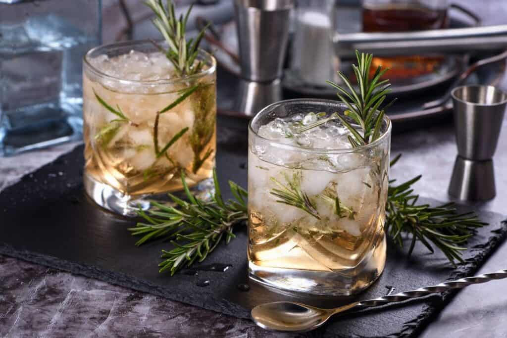Two glasses of iced drinks with rosemary sprigs.