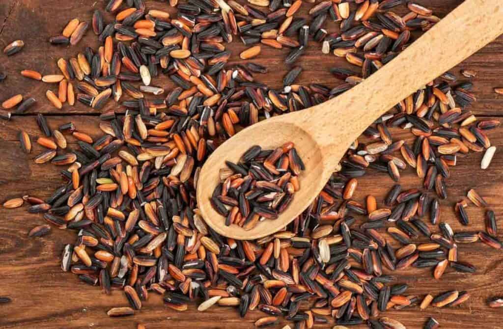 Mixed wild rice with a wooden spoon on a wooden table.