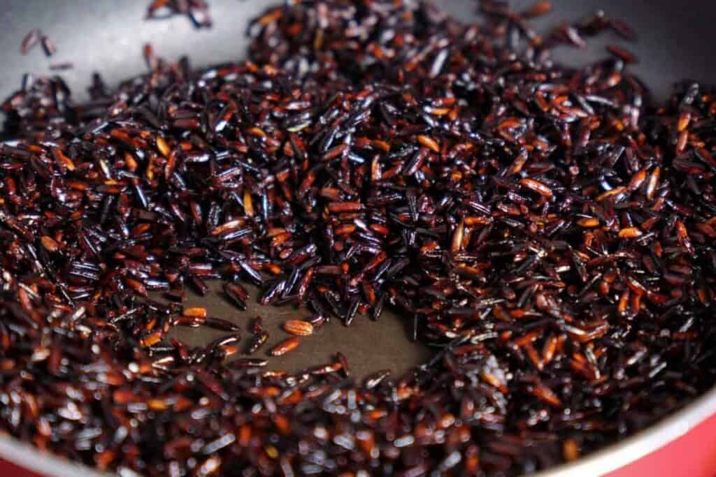 Fried rice grains in a pan, appearing burnt or possibly a variety of black rice.