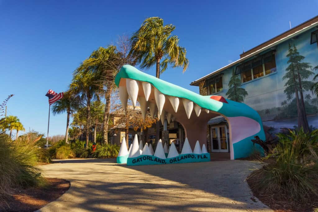 Entrance of gatorland, orlando, featuring a large alligator mouth-shaped archway, with palm trees and a clear blue sky in the background.