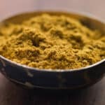 A close-up of a bowl filled with cumin on a wooden surface.