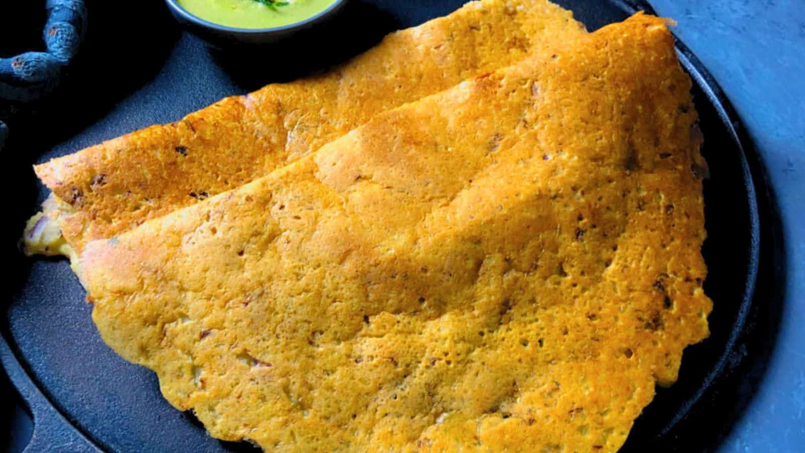 A crispy, folded masala dosa served on a black plate with a side of coconut chutney.