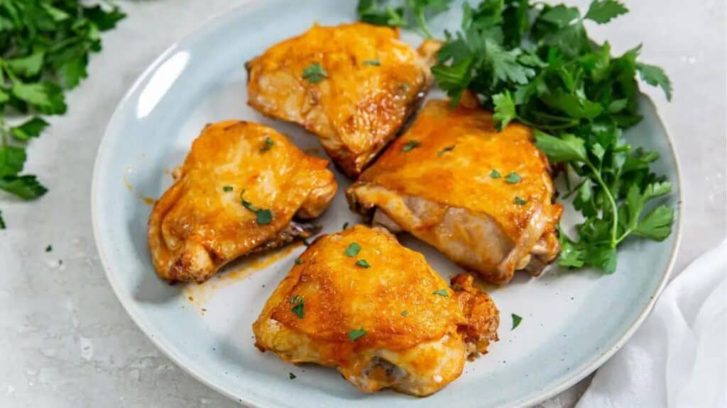 Air fryer buffalo chicken thighs garnished with parsley on a light blue plate, on a gray surface.