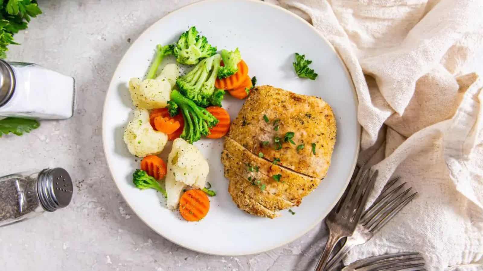 Air Fryer Chicken Cutlets on a white plate with parsley, carrots, broccoli, and cauliflower.