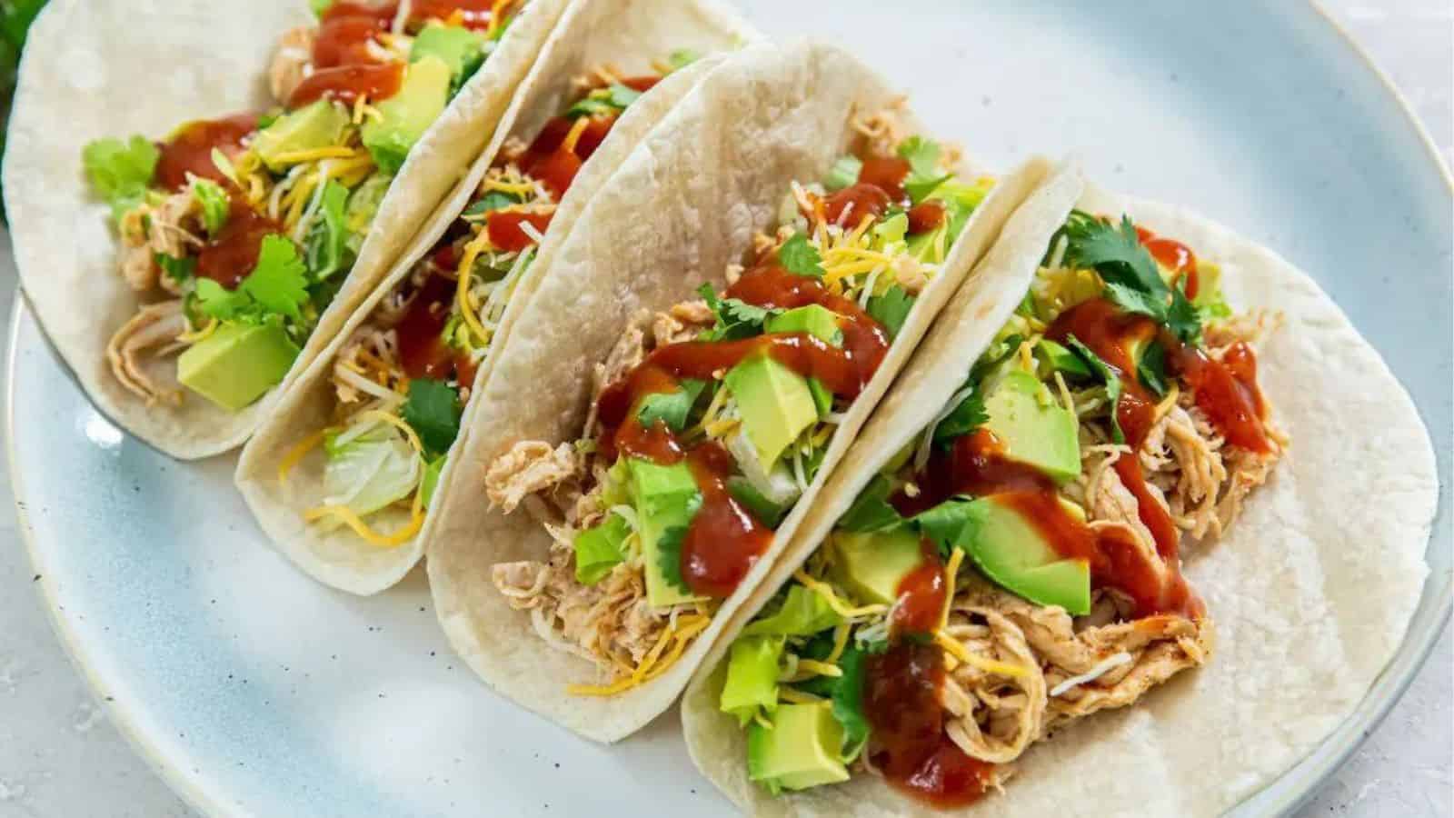 Air Fryer Chicken Tacos on a light blue plate with cheese, avocados, cilantro, and red sauce.