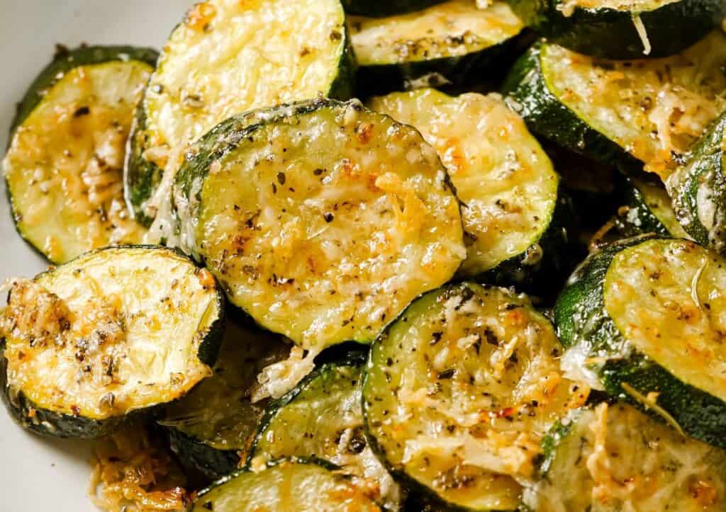 Close-up of roasted zucchini slices seasoned with herbs and grated cheese.