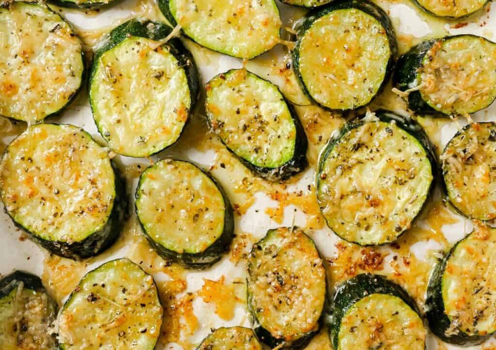 Roasted zucchini slices seasoned with herbs and cheese on a baking sheet.