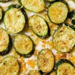 Roasted zucchini slices seasoned with herbs and cheese on a baking sheet.