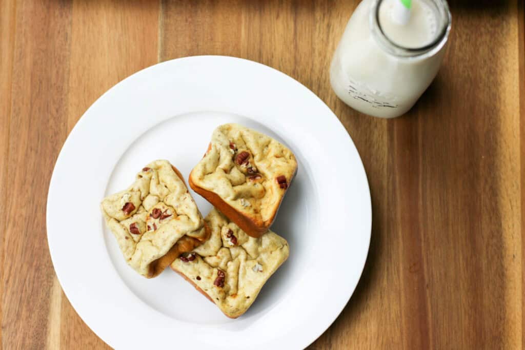 Three square pecan cookies on a white plate with a bottle of milk in the background, placed on a wooden table.