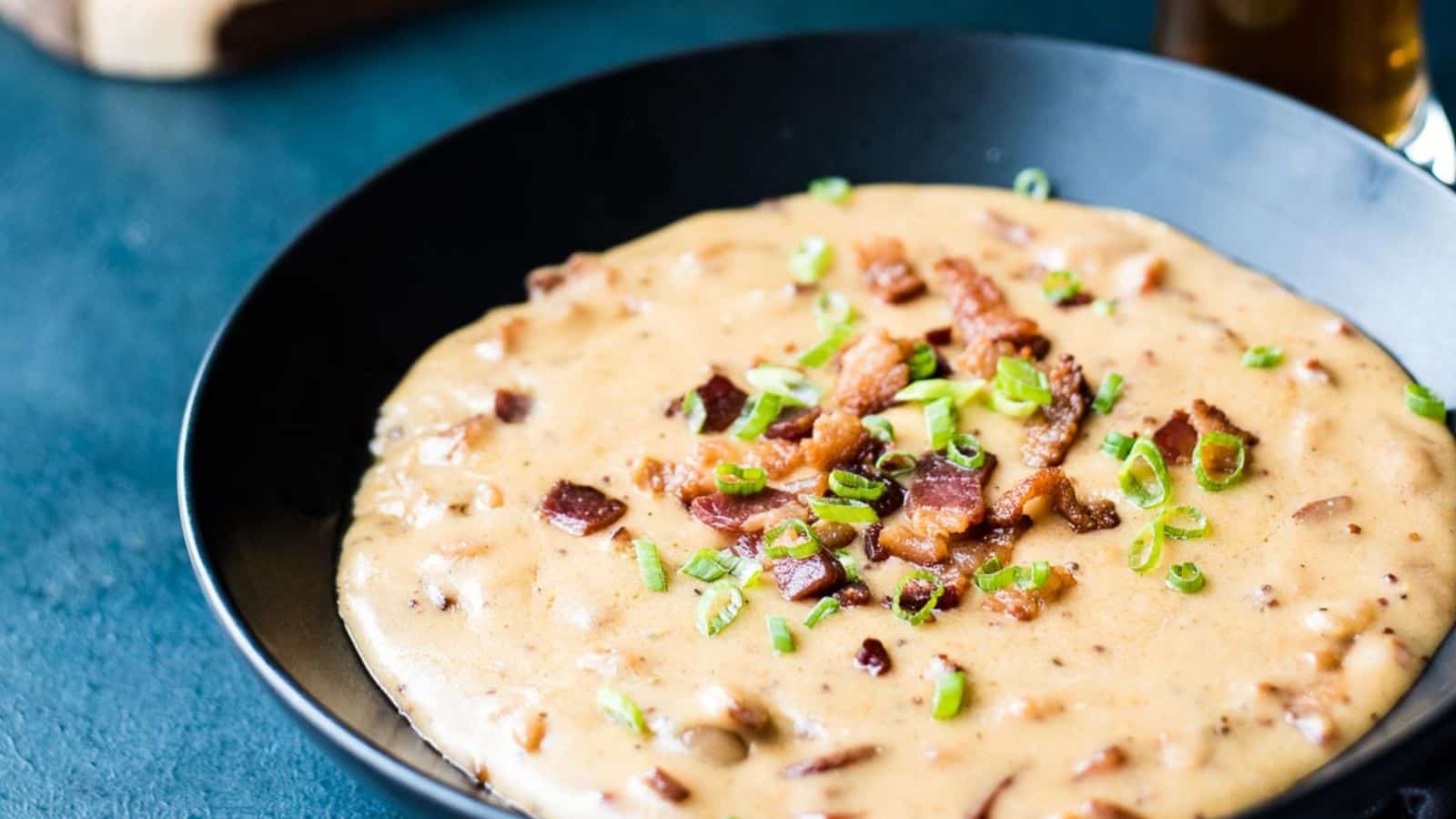 Bacon beer cheese in a dark bowl surrounded by pretzel knots on a cutting board.