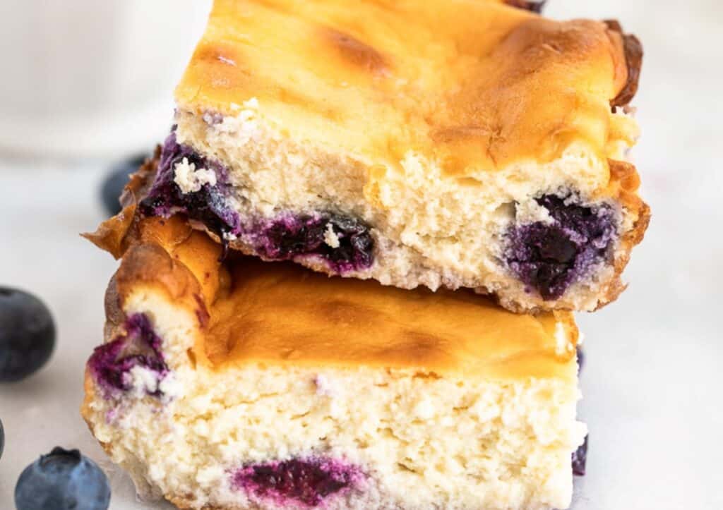 A close-up of a blueberry cheesecake bar with a golden-brown top.