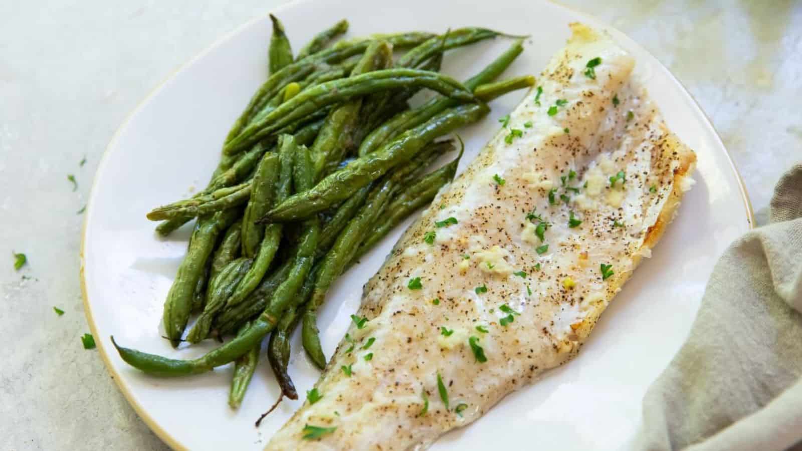 Broiled Walleye on a white plate with green beans, parsley, garlic, salt, pepper, and a fork.