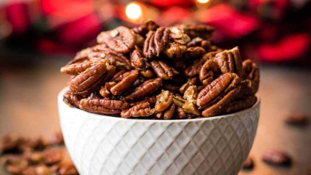 A bowl full of pecans with a festive background.